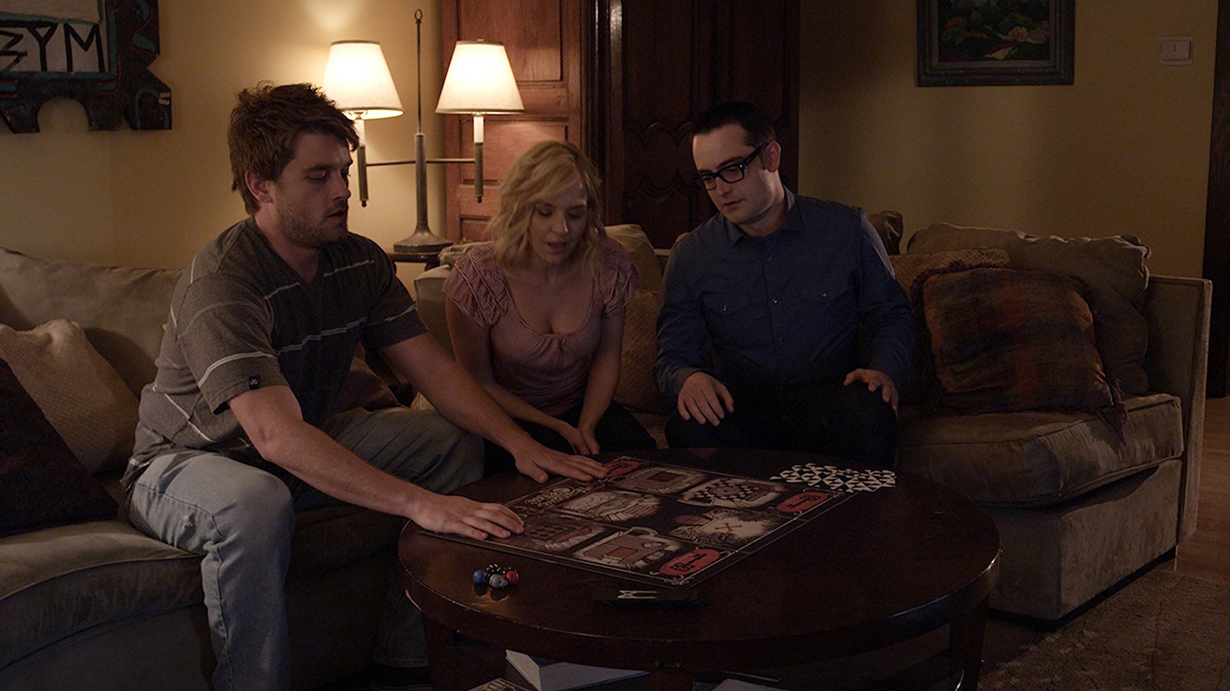 Brothers Chase Williamson and Graham Skipper with the latter's girlfriend Brea Grant sit down to play the video boardgame in Beyond the Gates (2016)