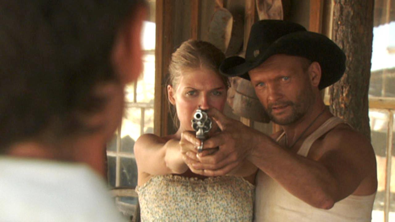 Andrew Howard shows Tess Panzer how to aim a gun in Blood River (2009)