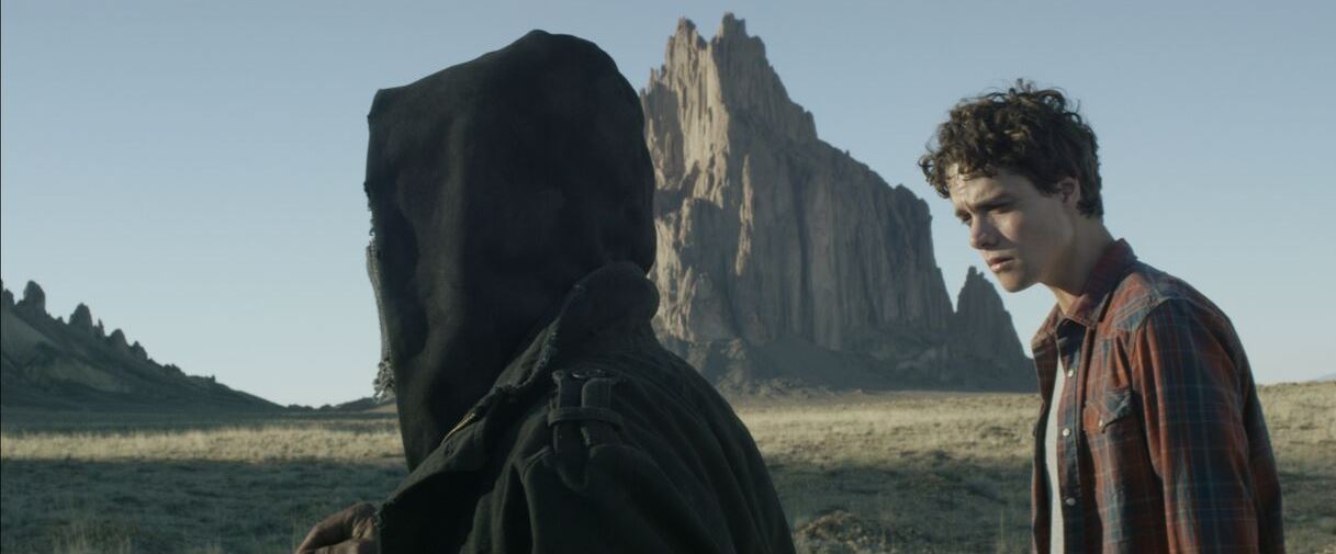 Douglas Smith is taken to an unmarked grave site in the desert by a mysterious hooded figure in Bottom of the World (2017)