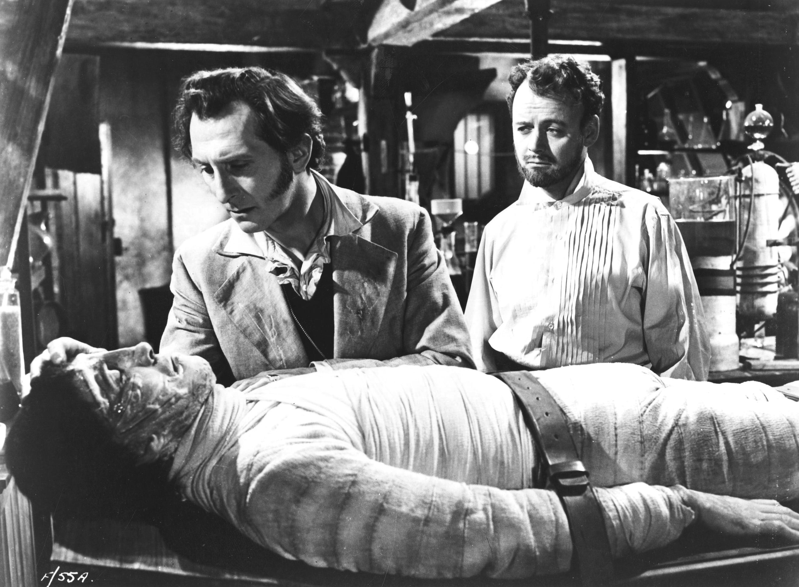 Baron Frankenstein (Peter Cushing) (l) and assistant Robert Urquhart (r) contemplate his monster (Christopher Lee) (foreground) in The Curse of Frankenstein (1957)