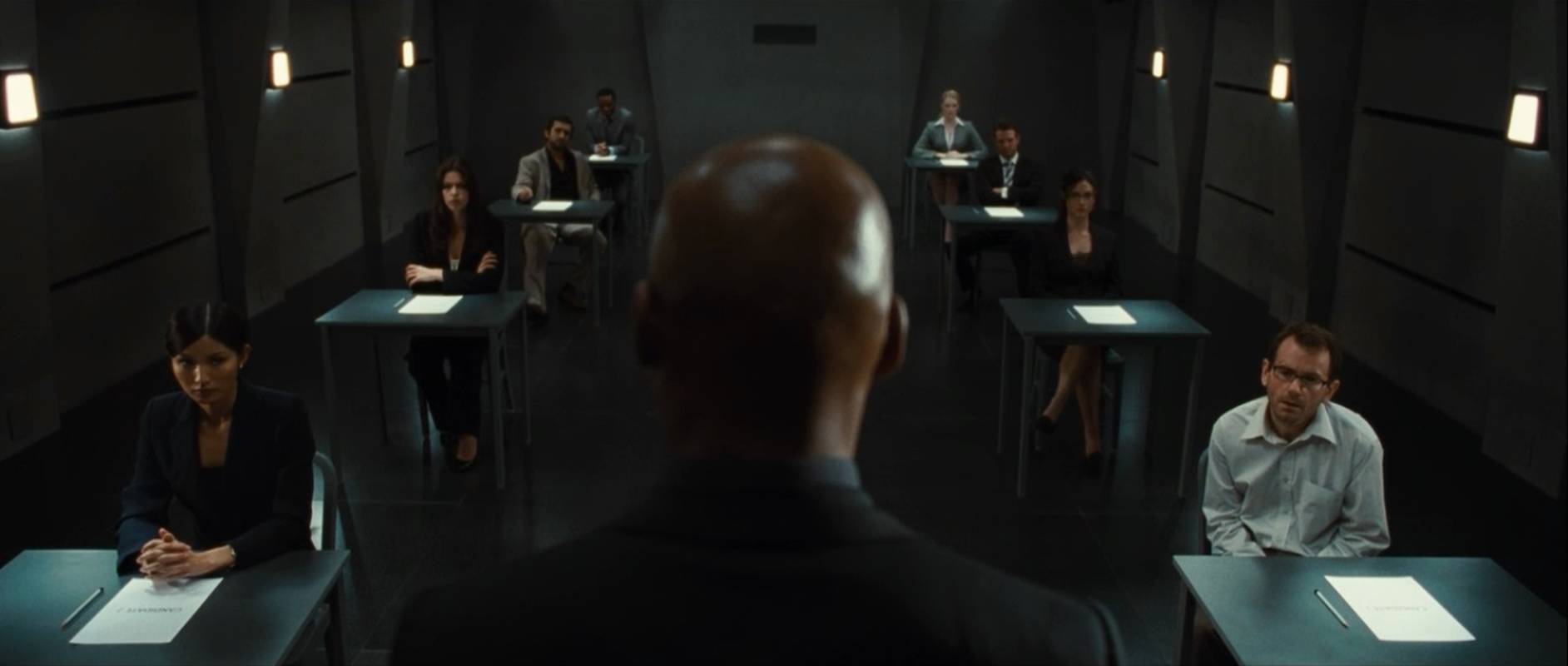 The Invigilator (Colin Salmon) (c) sets the exam for the applicants - (clockwise from left) Gemma Chan, Pollyanna McIntosh, Jimi Mistry, Chukwudi Iwuji, Nathalie Cox, Luke Mably, Adar Beck and John Lloyd Fillingham in Exam (2009)