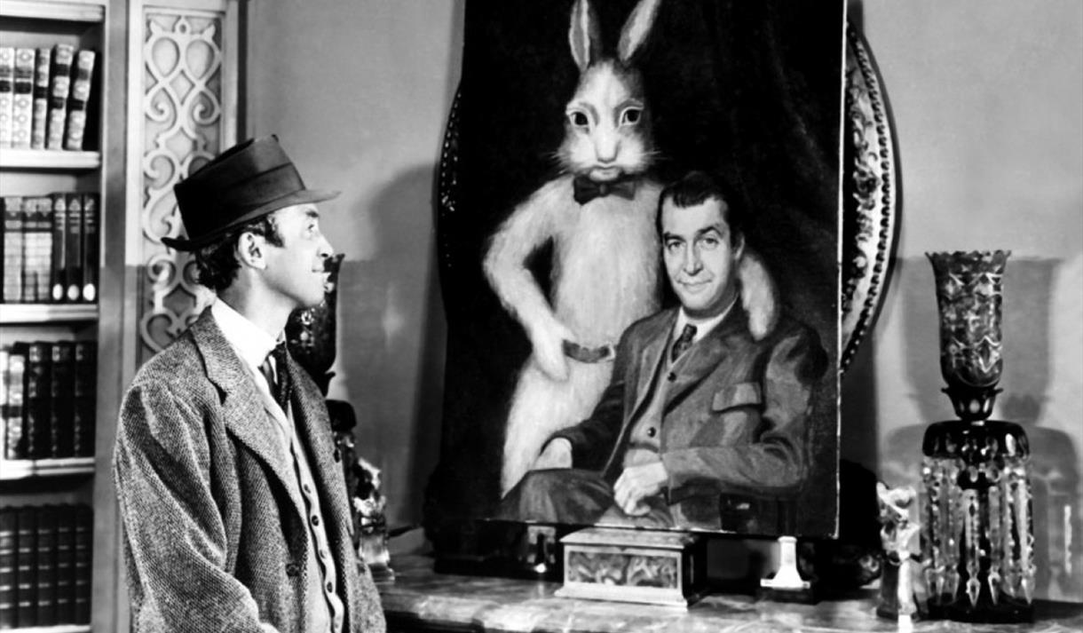 Elwood P. Dowd (James Stewart) looks affectionately on at the portrait of himself and Harvey in Harvey (1950)