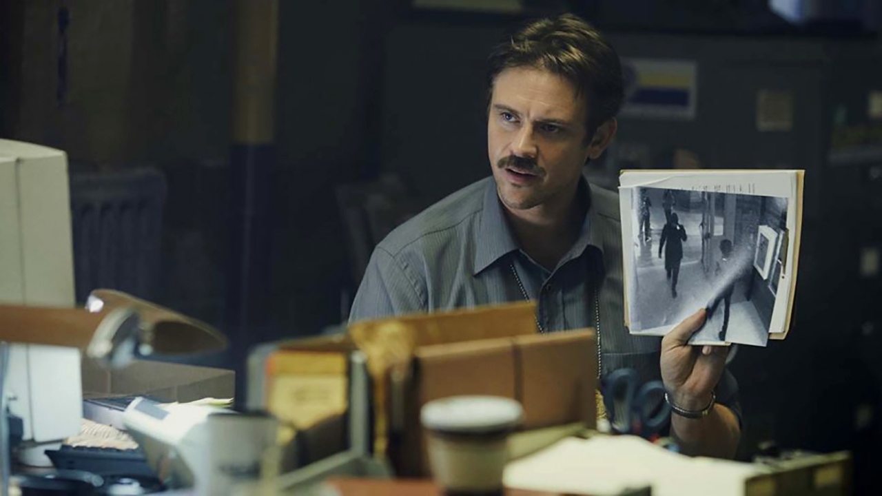 In 1997, detective Boyd Holbrook holds up a surveillance camera picture of mystery girl Cleopatra Coleman in In the Shadow of the Moon (2019)