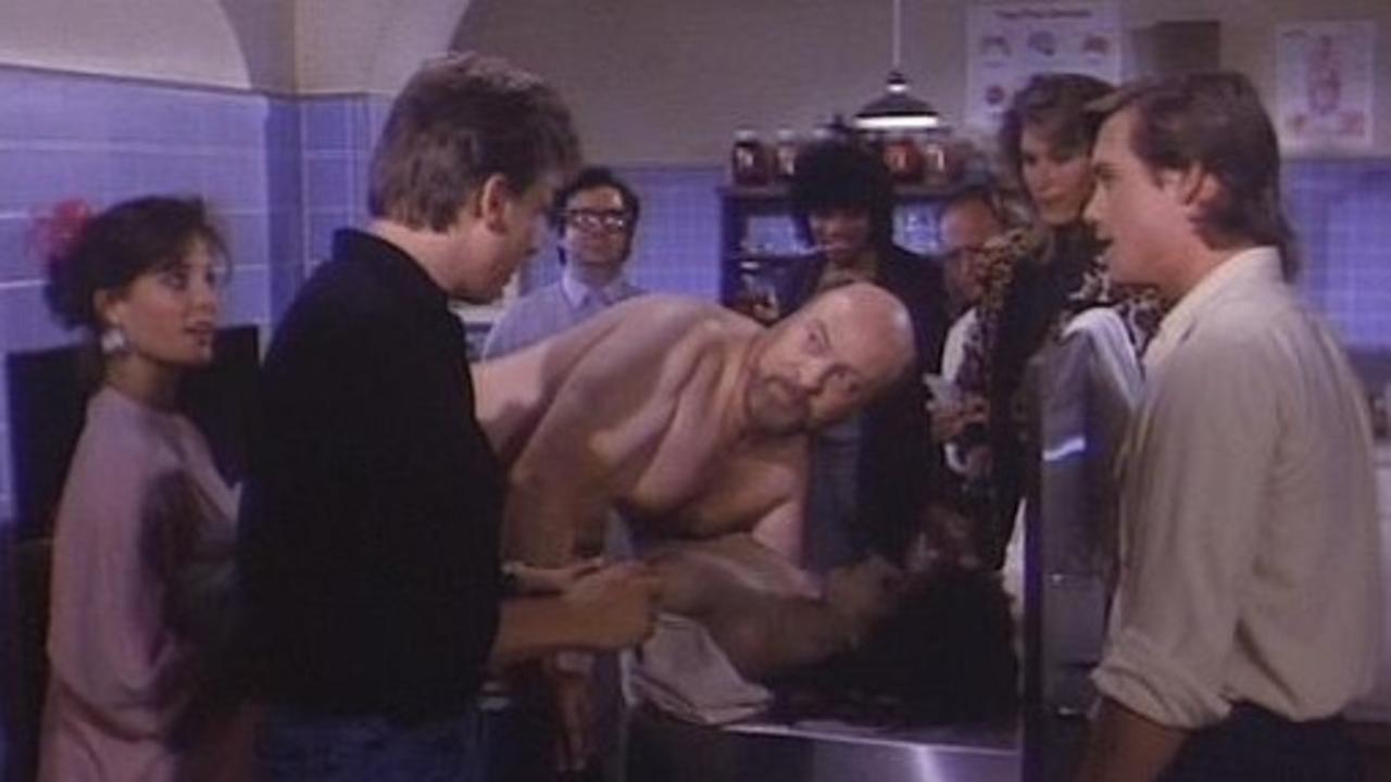 Paul Bartel (c) demonstrates his penchant for necrophilia, flanked by (l to r) Lynn Danielson, Perry Lang (back to camera in black shirt), Mary Woronov (in leopard skin) and Christopher Atkins (to her right) in Mortuary Academy (1988)