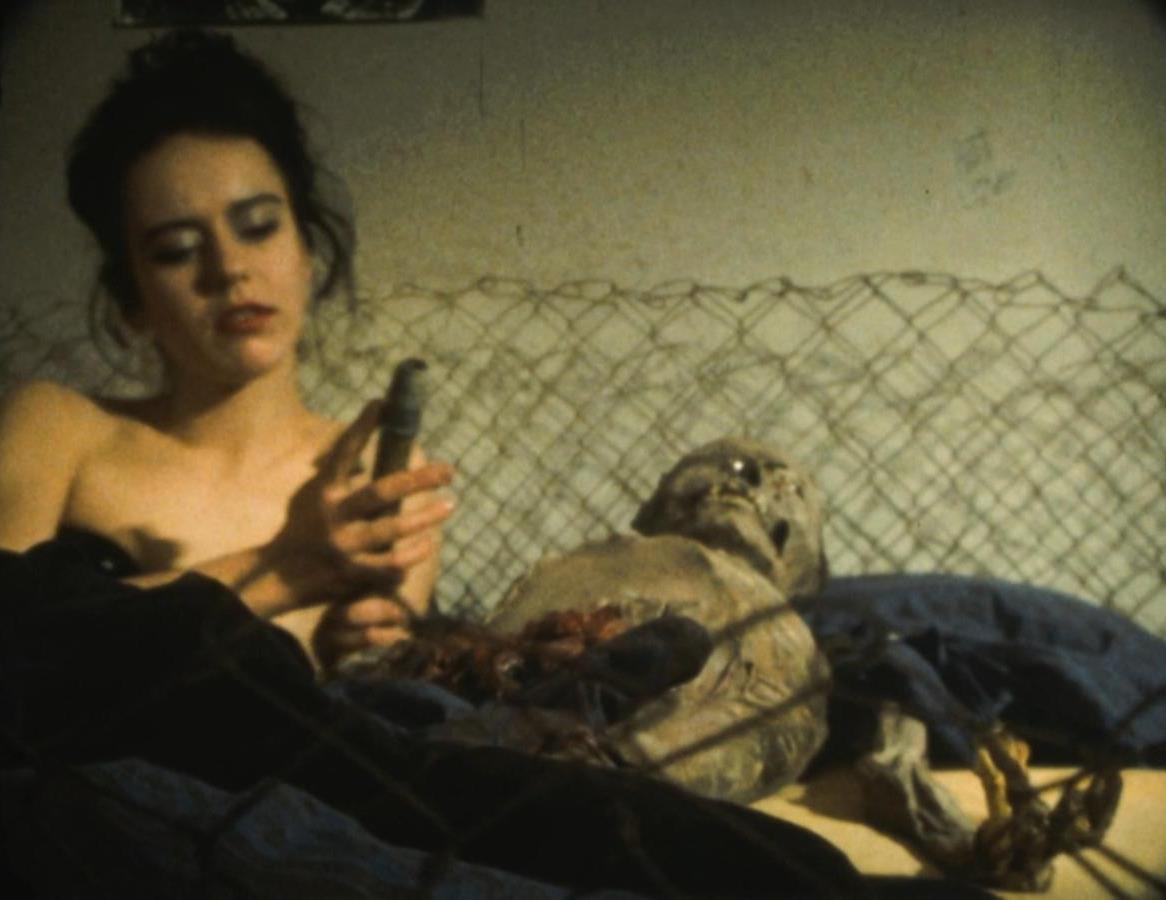 Beatriz M outfits the corpse with condom covered dowling for a spot of necrophilia in NEKRomantik (1987)