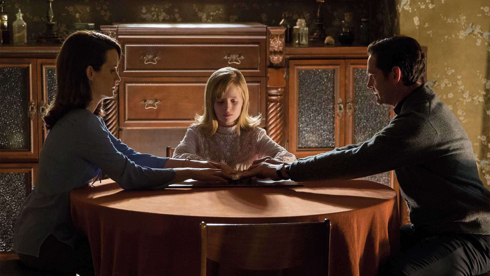 Elizabeth Reser, Lulu Wilson and Henry Thomas sit down to a seance in Ouija Origin of Evil (2016)