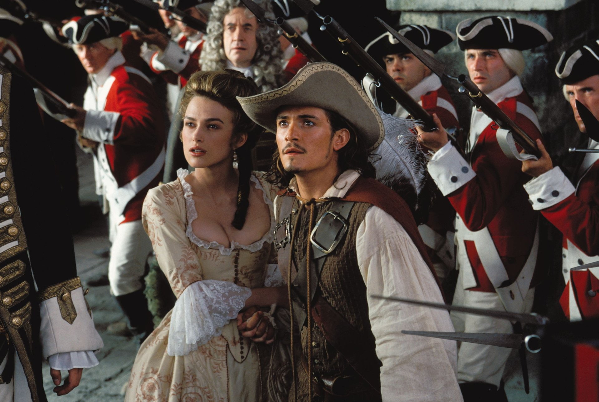 Elizabeth Swann (Keira Knightley) and Will Turner (Orlando Bloom) with the British Navy and Governor Swann (Jonathan Pryce) behind her in Pirates of the Caribbean: The Curse of the Black Pearl (2003)