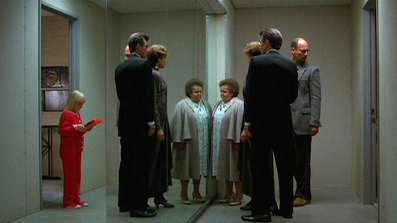 An example of the eerie mirror effects - Carole Ann (Heather O'Rourke - in red on left) and on the other side of the mirror (l to r) Tangina (Zelda Rubinstein), Nancy Allen and Tom Skerritt (back to camera) and psychologist Richard Fire in Poltergeist III (1988)