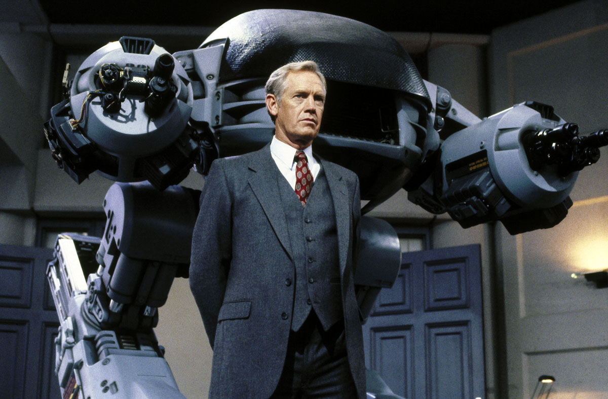 Dan O’Herlihy as The Old Man, flanked by the ED-209 in Robocop (1987)