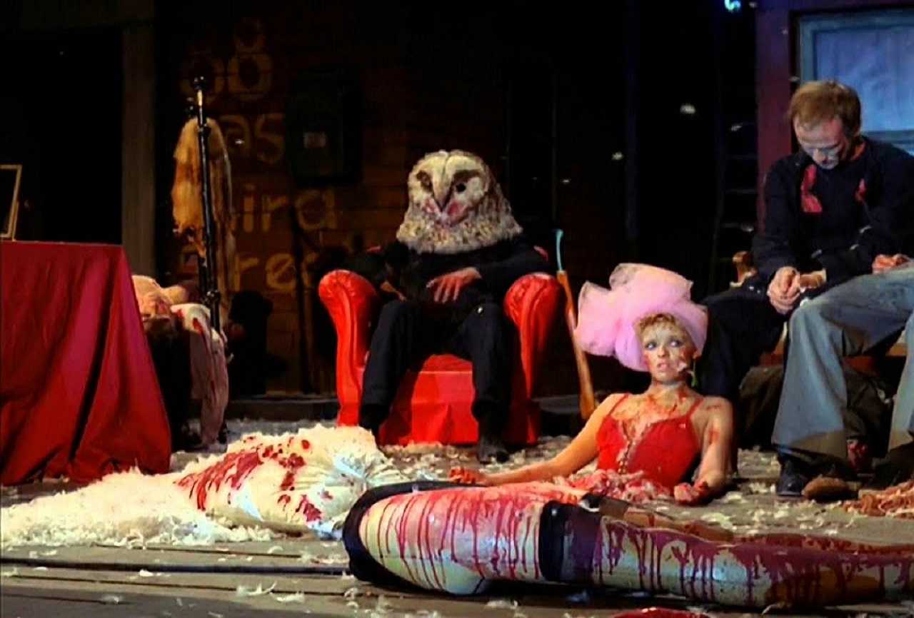 The owl-masked killer sits amid a stage filled with dead bodies in StageFright - Aquarius (1987)