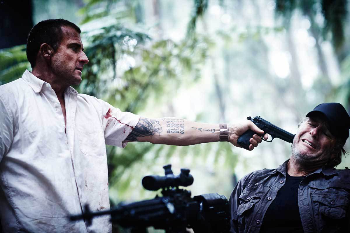 Dominic Purcell as Rick Tyler, a Navy SEAL forced into a barehands survival game, holds a gun to hunter Robert Taylor in Turkey Shoot (2014)