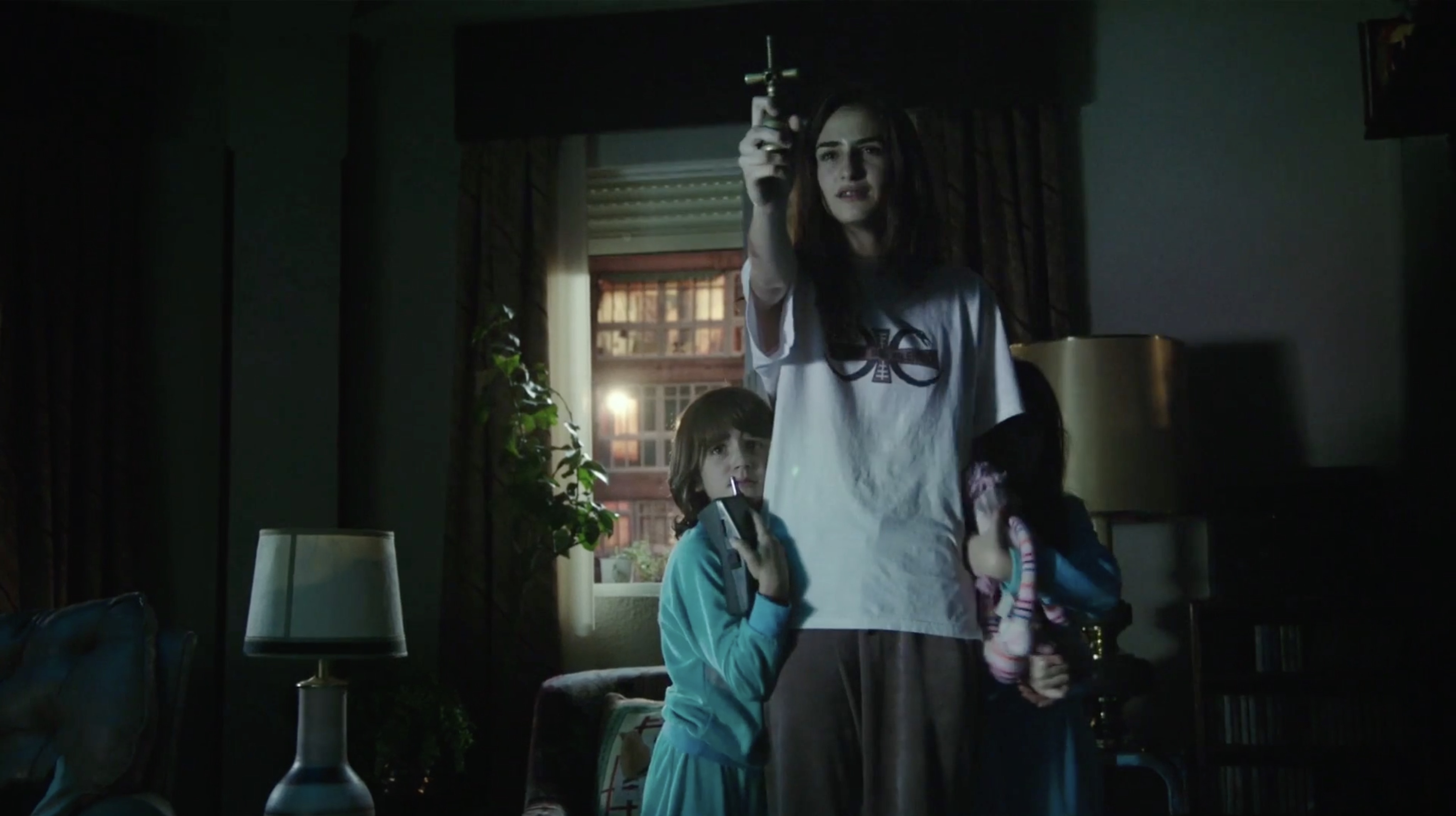 Veronica (Sandra Escacena) (c) holds up a crucifix to ward off evil while protecting her sisters Bruna Gonzalez (l) and Claudia Placer (r) in Veronica (2017)