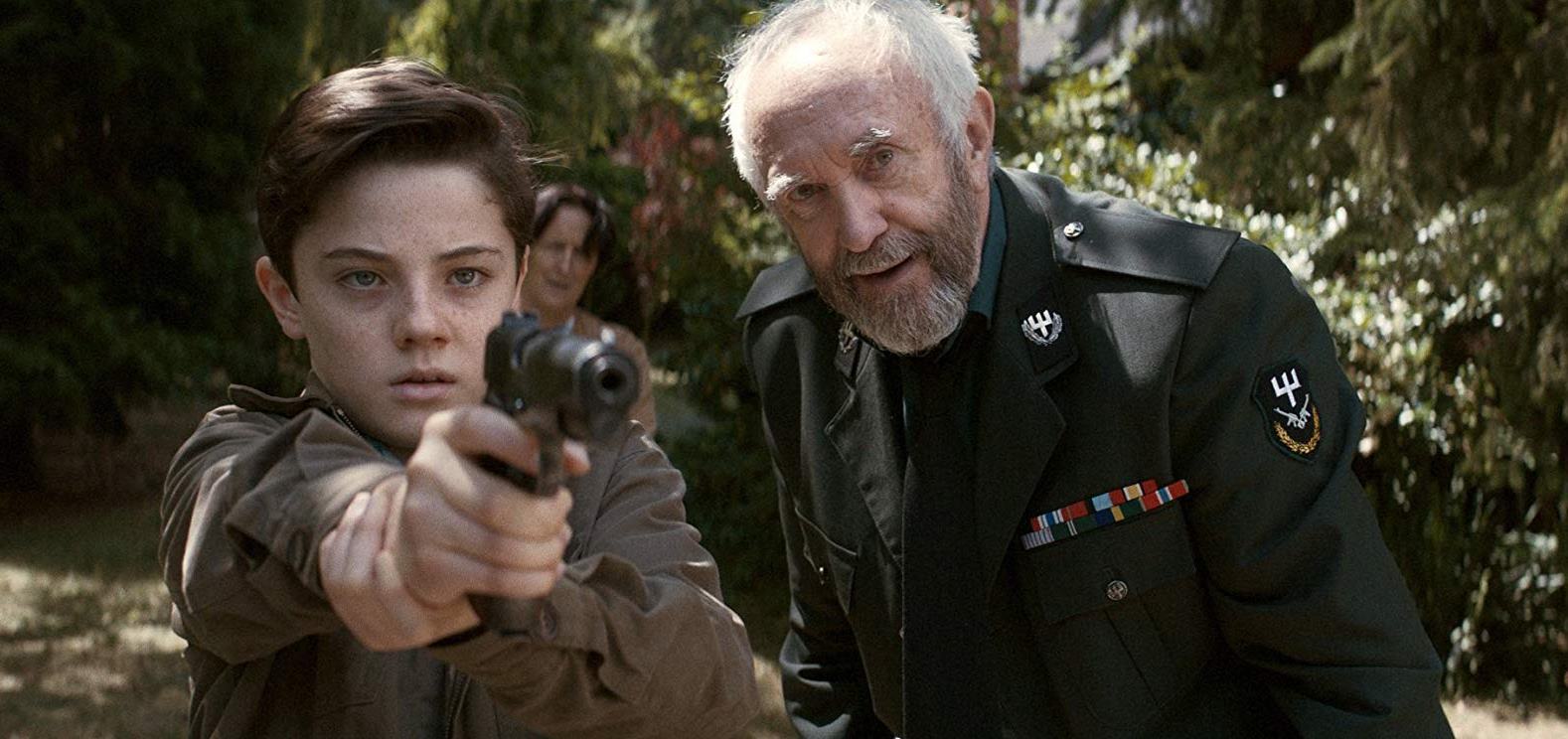 Young Djarta (Lorenzo Allchurch) is taught how to use a gun by his grandfather Jonathan Pryce. With grandmother Fiona Shaw lurking in the background in The White King (2016)