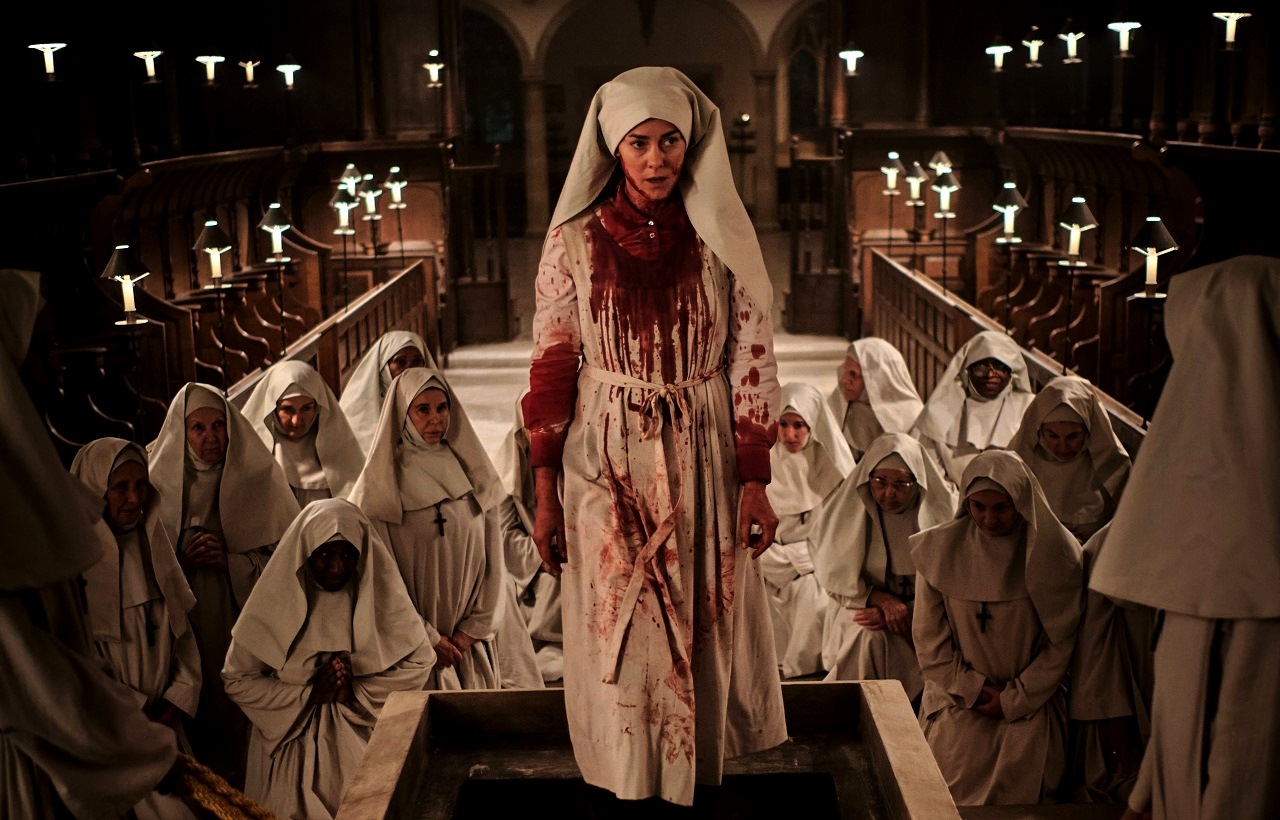Jena Malone in bloody surplice among the nuns of the convent in Consecration (2022)