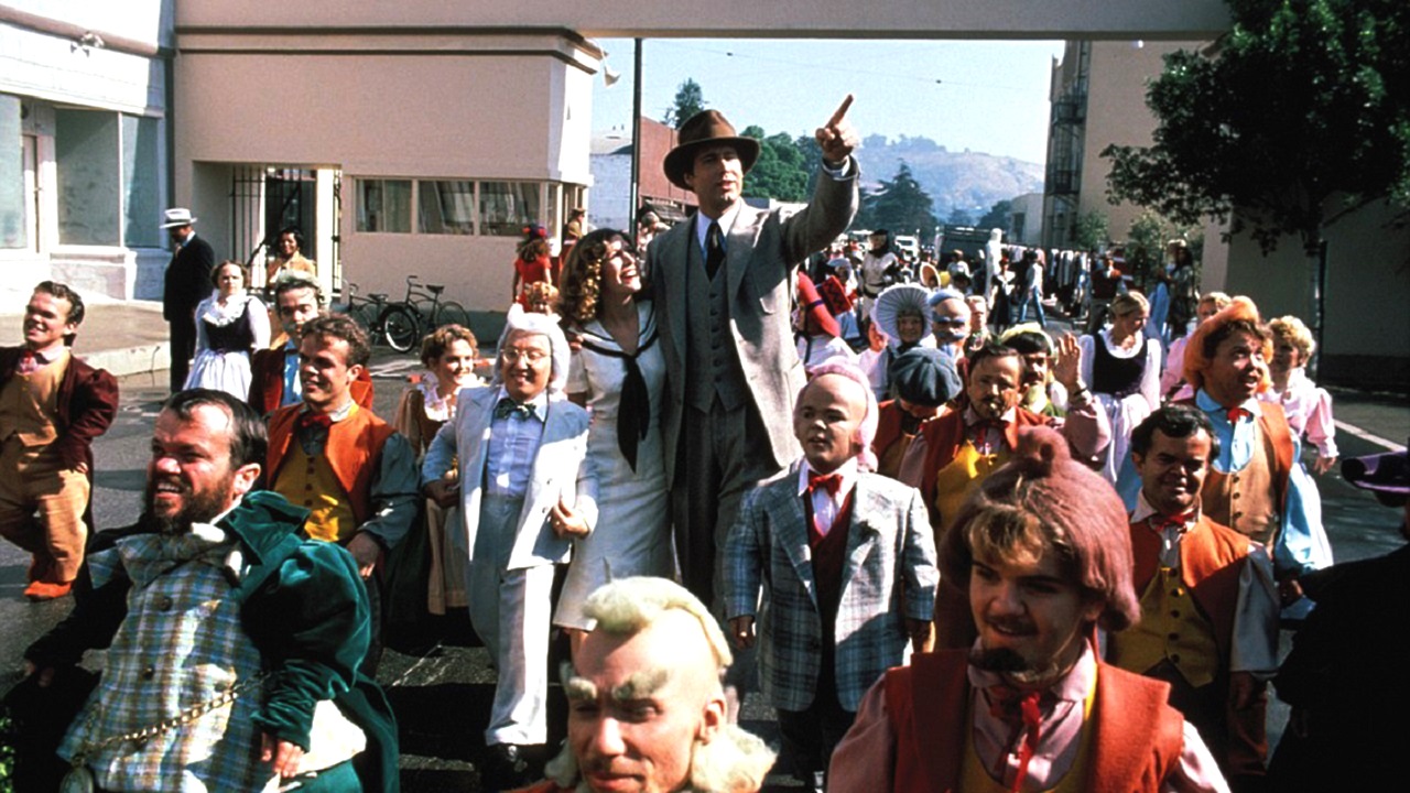 Carrie Fisher and Chevy Chase with the dwarfs on the studio backlot in Under the Rainbow (1981)